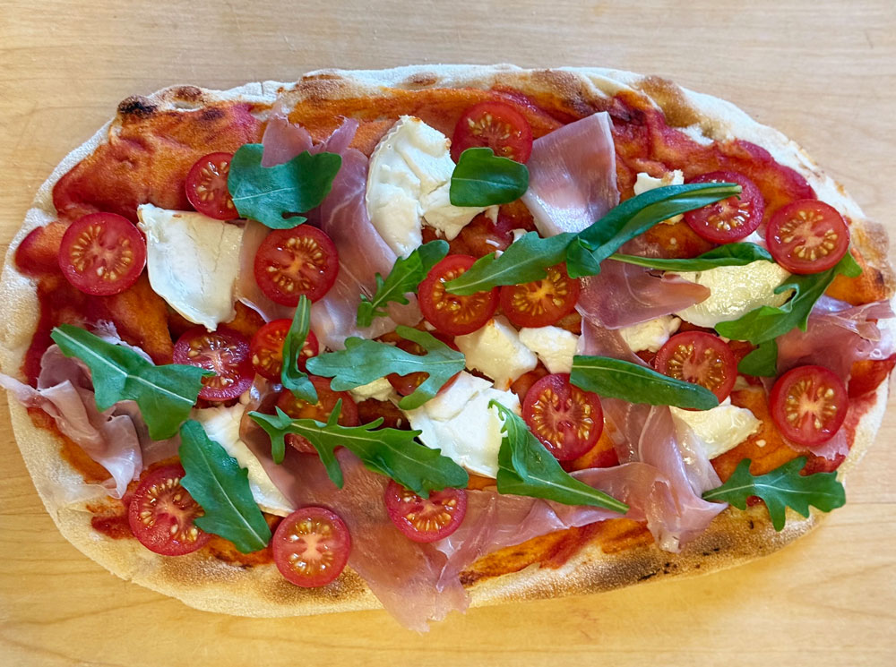 Pinsa ilmakuivatun kinkun, vuohenjuuston, tomaatin ja rucolan kanssa. Pinsa con crudo